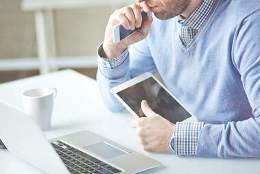 A man holding a cell phone and looking at an ipad.