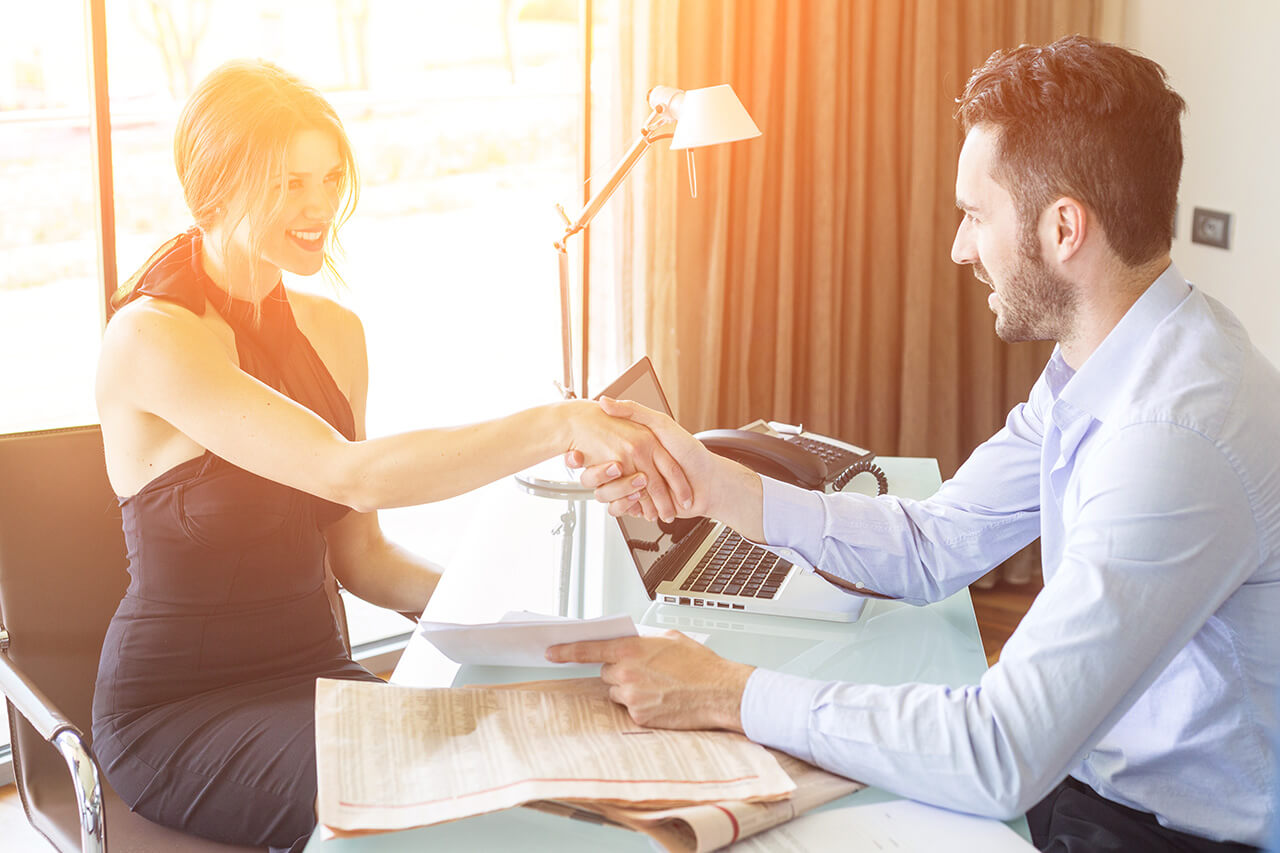 A man and woman shaking hands over a desk.